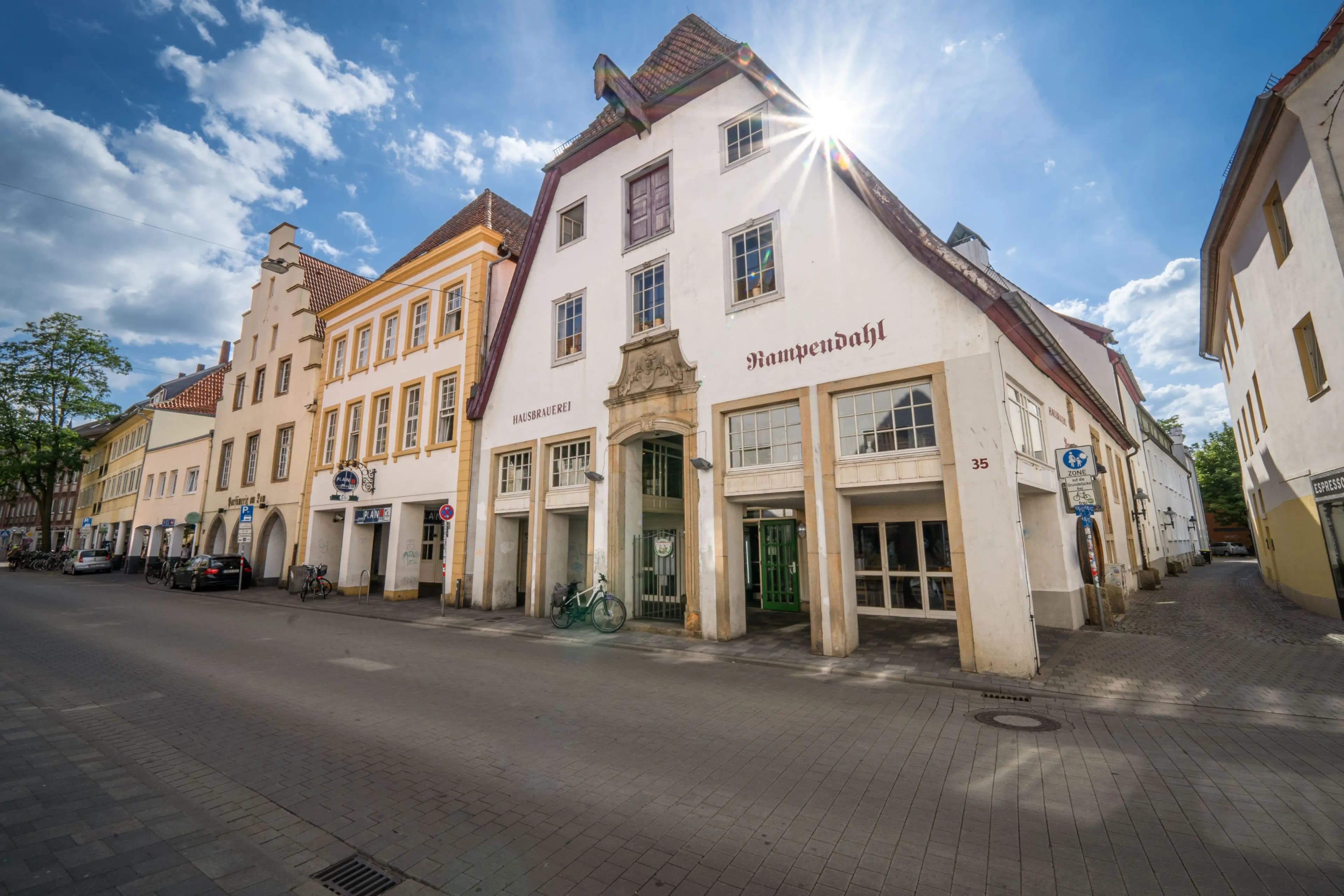 Historische Gebäudezeile mit dem Haus Kampendahl, dessen Giebel von der Sonne angestrahlt wird, an einer gepflasterten Straße.