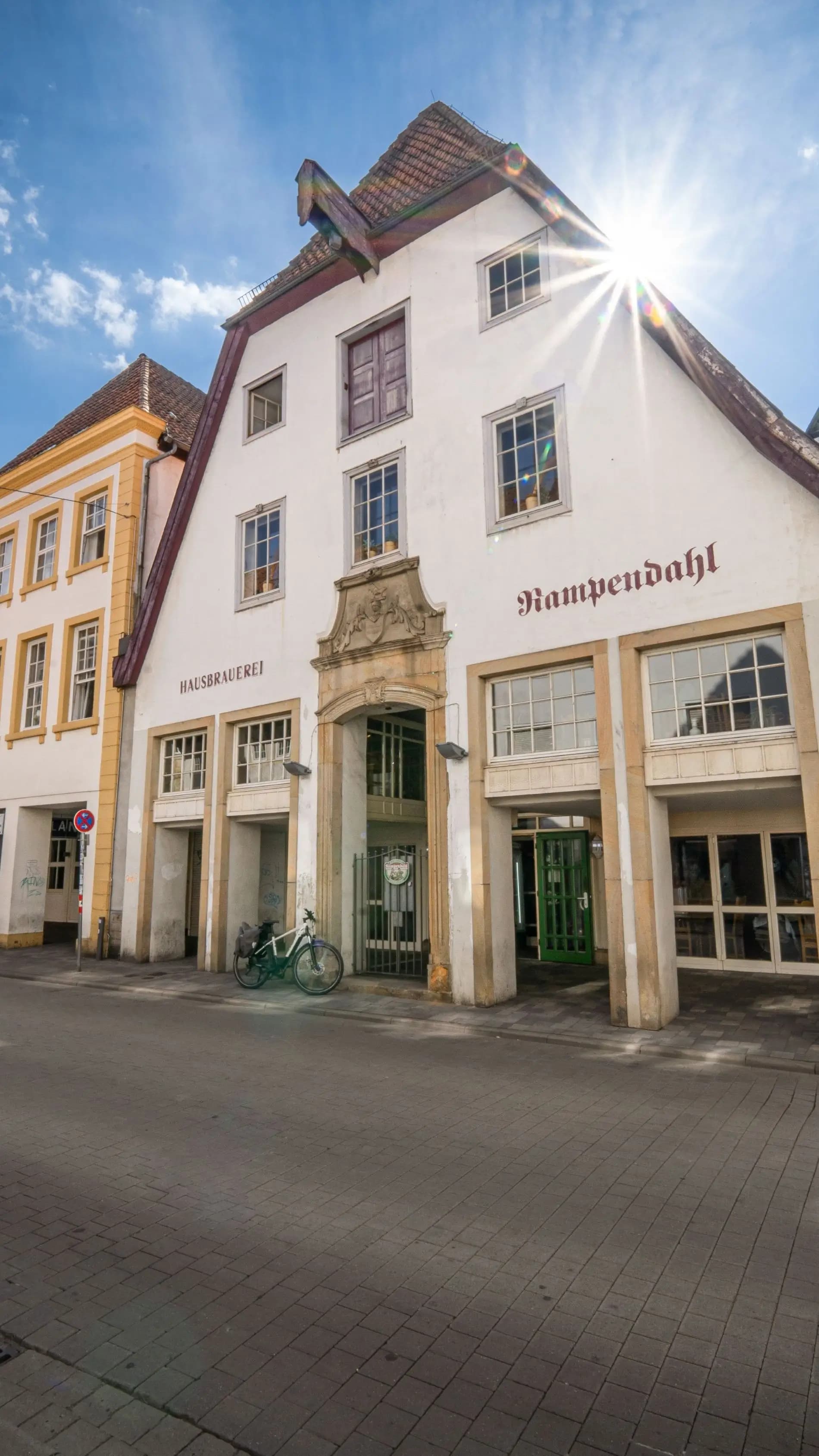 Historische Gebäudezeile mit dem Haus Kampendahl, dessen Giebel von der Sonne angestrahlt wird, an einer gepflasterten Straße.